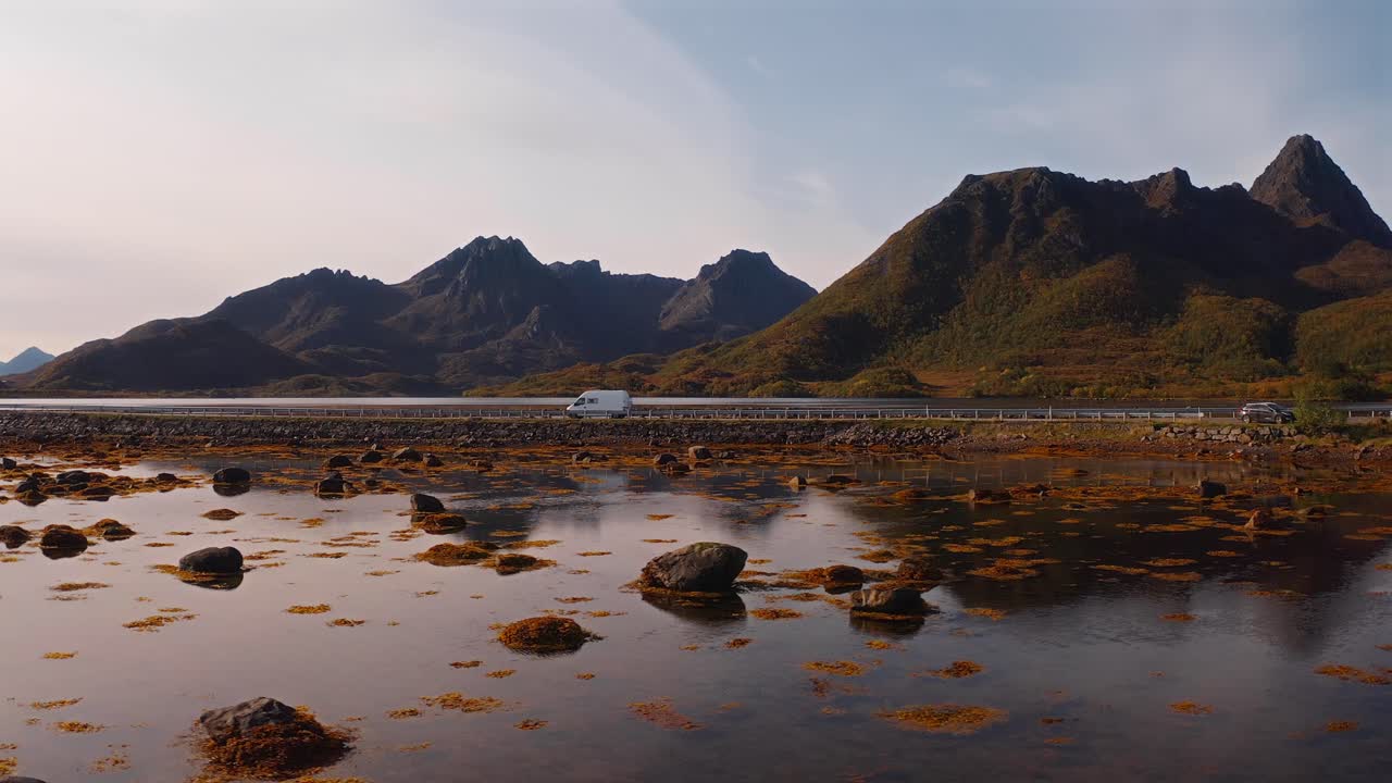 A scenic shot of a van driving along a coastal road in Vestarelen, Norway, surrounded by mountains