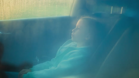 una joven se sienta en el asiento trasero de un coche, mirando por la ventana.