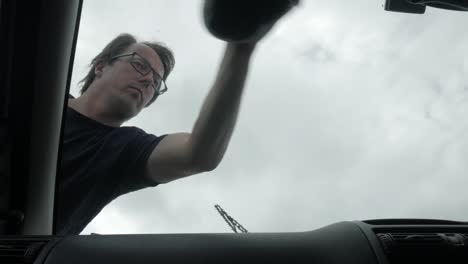 man scrubbing the front glass window of his vehicle