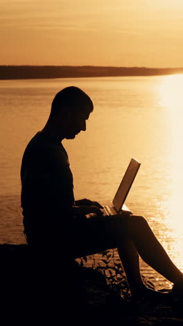 man sit and work on the laptop by sunset (sunrise) background on the top of the hill. vertical video
