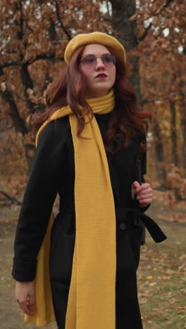 turista enfocada en muffler amarillo y boina camina por el bosque, ajustando el cabello y sosteniendo la correa de la bolsa, profundamente inmersa en su viaje