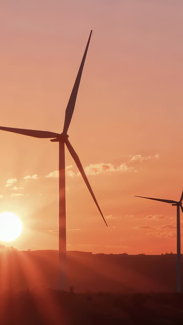 Vertical video: Spinning three-blade turbine rotating from wind at sunset on hills, with lens flare