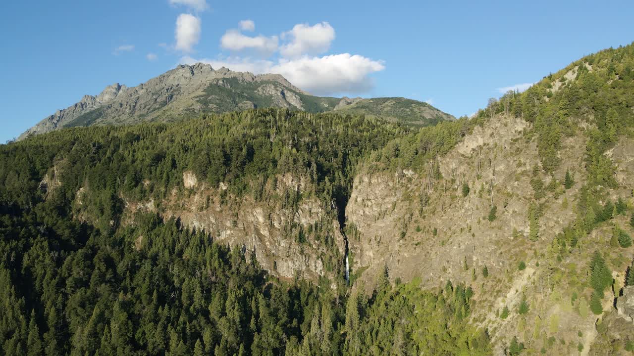 toma de órbita aérea de la cascada corbata blanca entre montañas andinas y bosques de pinos, patagonia argentina