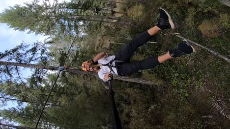 vertical action camera shot of a young man sitting with legs out as he goes down the zipline very fast