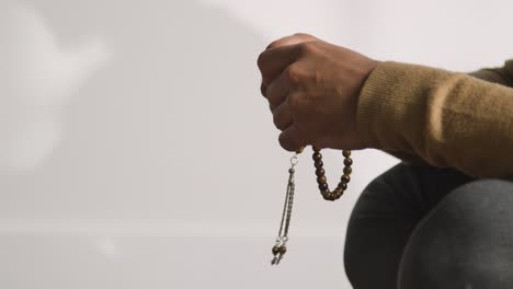 close up of muslim man praying holding prayer beads casting shadow on wall behind