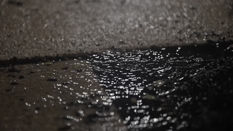 grimy puddle on sidewalk in rainfall with rippling water