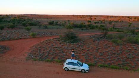 orbiting aerial view of a man standing on a car in the middle of australian outback - northern territory australia