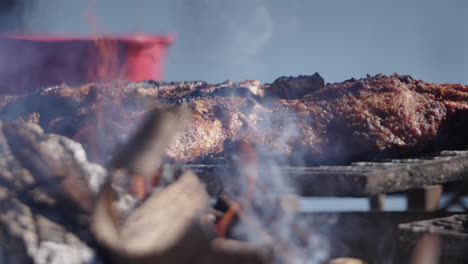 asado argentino steak base grilling over open fire with visible flames and smoke.