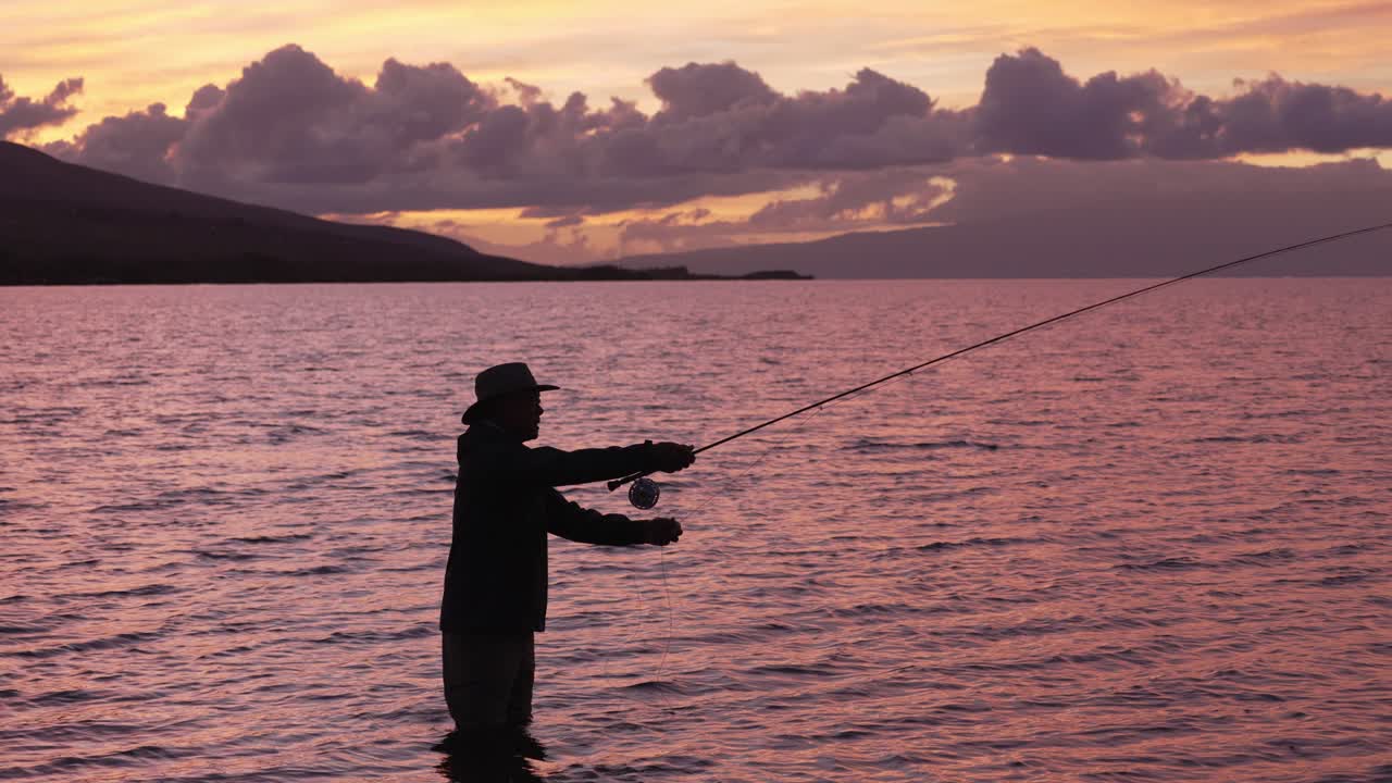 Gerak lambat digunakan untuk menunjukkan bidikan penuh pemancing lalat dalam siluet saat matahari terbenam di Molokai, Hawaii.
