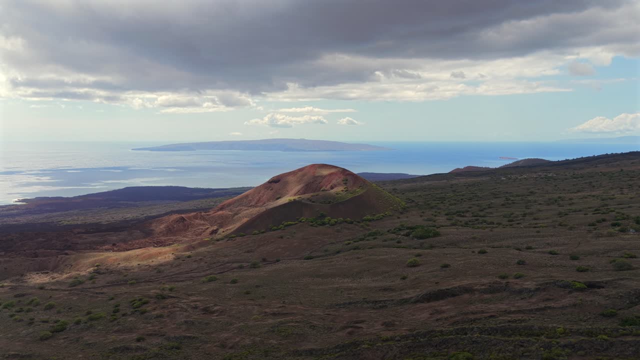 Aerial view of a Maui volcanic cinder cone with sweeping terrain, striking light moving through clouds and a clear ocean panorama toward nearby Hawaiian islands