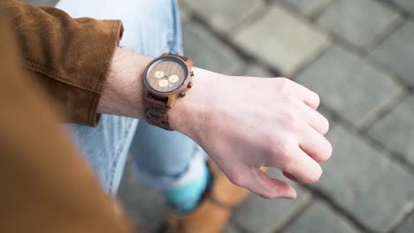 male wrist with a wooden fashionable watch and brown jacket,jeans,city