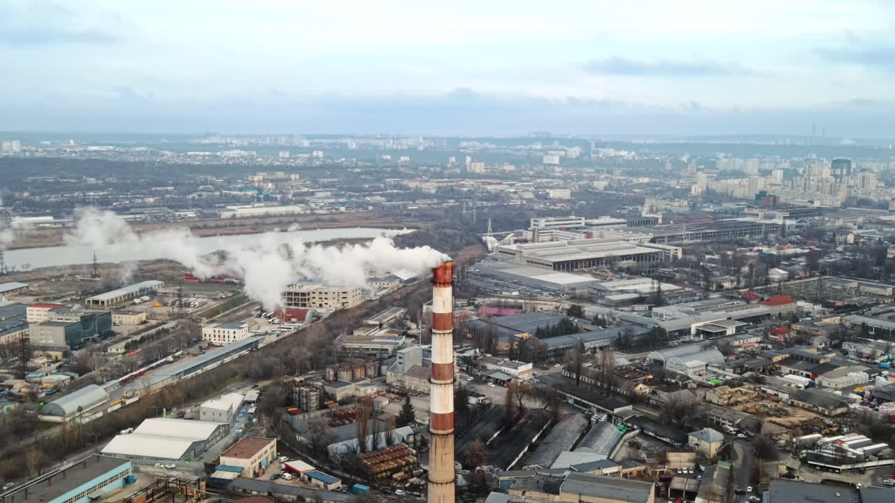 Aerial drone view of thermal station with smoke coming out of the tube. Buildings, roads, lake and bare trees on the background. Cloudy weather. Chisinau, Moldova