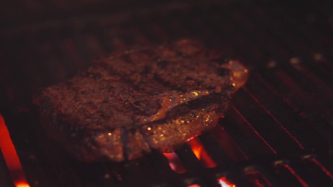 Cucina notturna all'aperto al barbecue con succulenta bistecca di controfiletto girata sulla griglia con grandi fiamme.