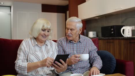 Senior-pensioner-couple-with-digital-tablet-pc-computer-at-home.-Resting-on-sofa-in-cozy-living-room