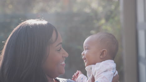 sonriente madre afroamericana acurrucada y jugando con su hija en el jardín en casa