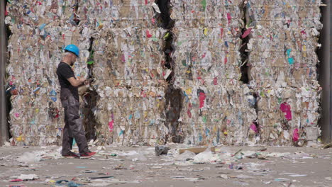 Manager-at-paper-recycling-plant-wearing-overalls-and-hard-hat-counts-bales