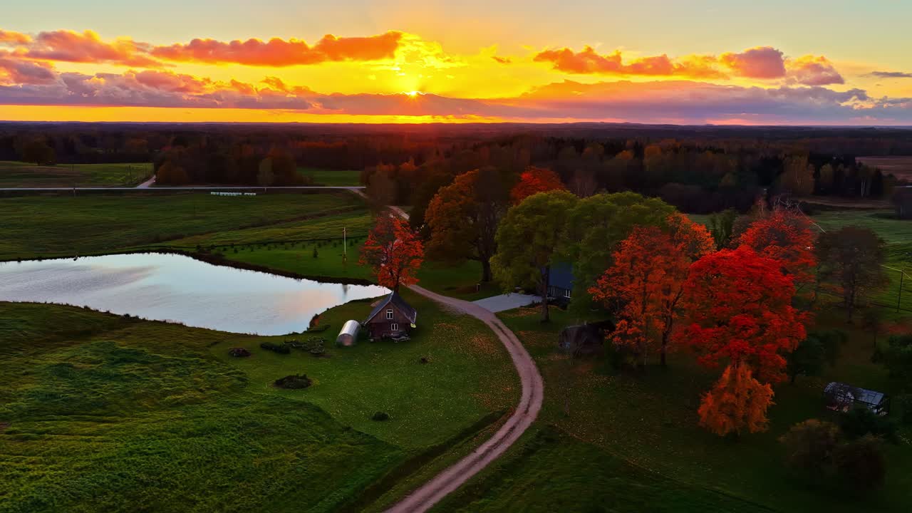 Aerea: tramonto con cielo infuocato su una foresta con un piccolo lago e una casa, ripresa in allontanamento da drone.