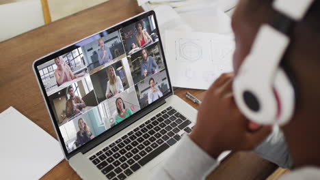 african american male college student wearing headphones having a video conference on laptop at home