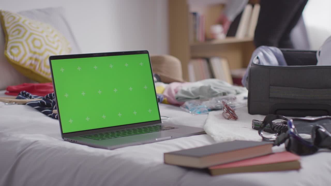 portátil de pantalla verde con una maleta de embalaje de persona en la cama en casa para las vacaciones de verano