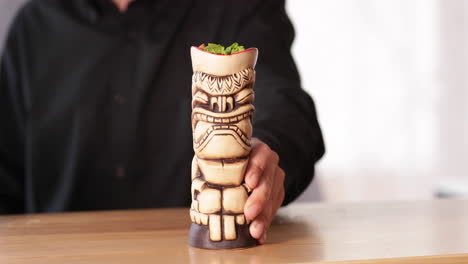 Barkeeper-Serving-Cocktail-Drink-In-A-Carved-Wooden-Tiki-At-The-Restaurant-Bar-Counter---close-up