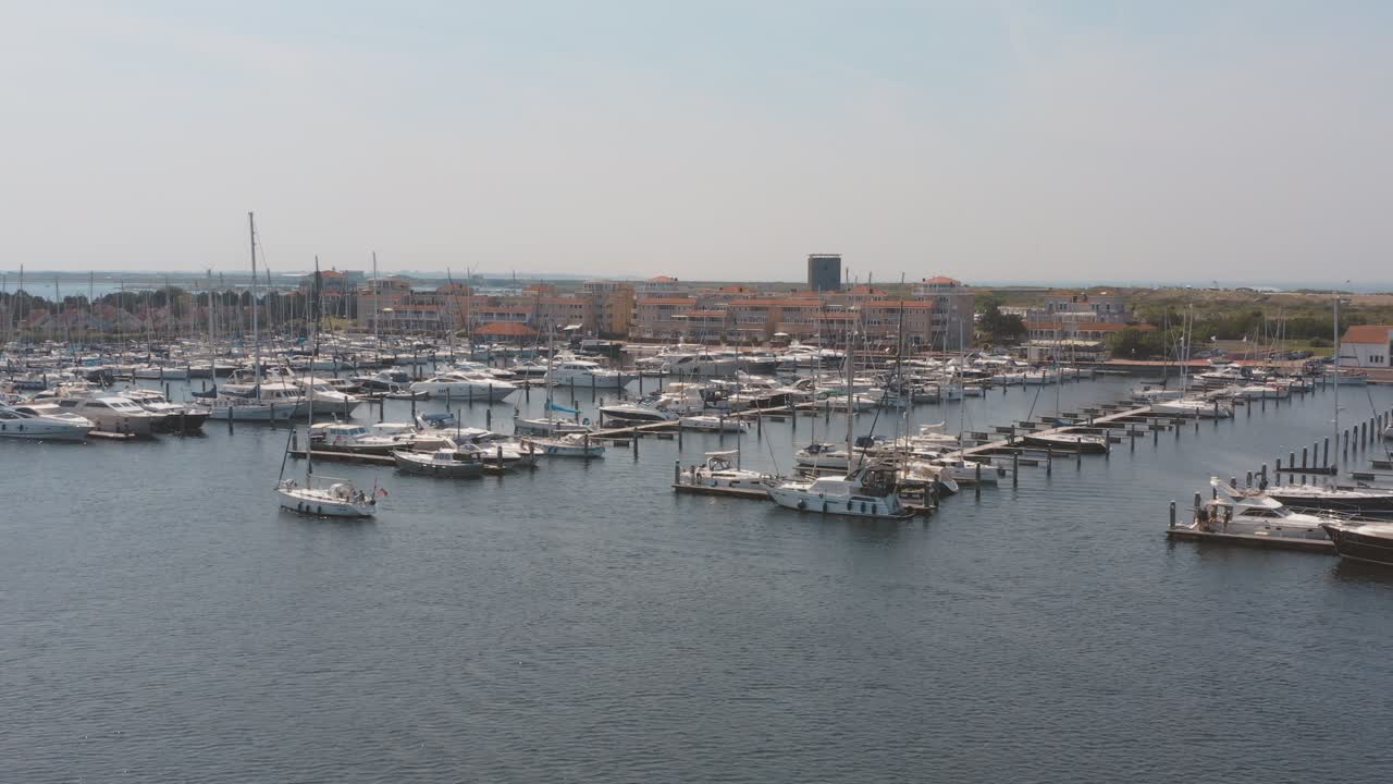 Cinematic drone - aerial panorama shot of a marina with sailing boats one boat sailing in the foreground on a sunny day at Zeeland at the north sea, Netherlands, 25p