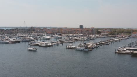 Cinematic-drone---aerial-panorama-shot-of-a-marina-with-sailing-boats-one-boat-sailing-in-the-foreground-on-a-sunny-day-at-Zeeland-at-the-north-sea,-Netherlands,-25p