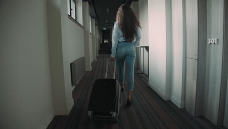 Young-woman-rolling-suitcase-in-hotel-corridor.-Slim-girl-crossing-hotel-space