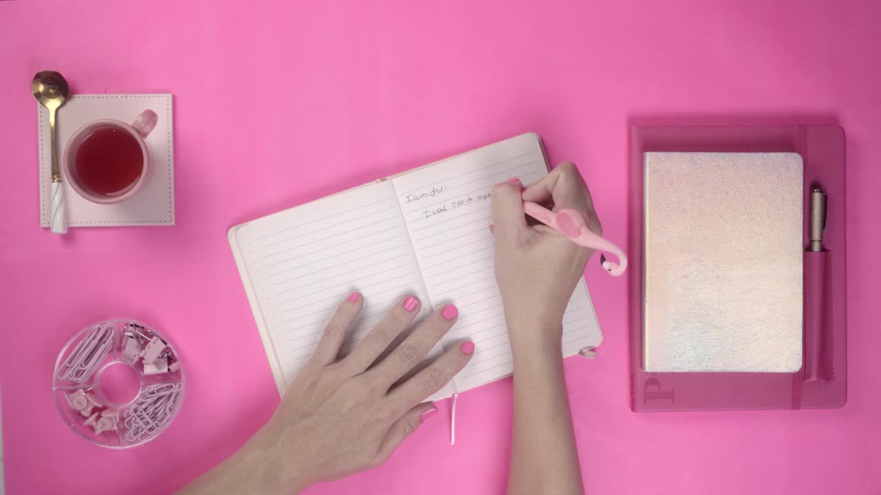 Overhead View of Hands Writing in Notebook on Pink Desk