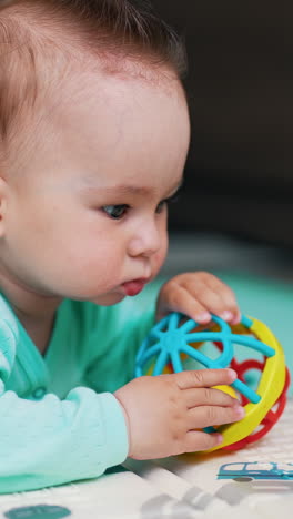 sweet little baby boy lies on the floor on his belly. adorable child in blue shirt plays with a bright ball. close up. vertical video