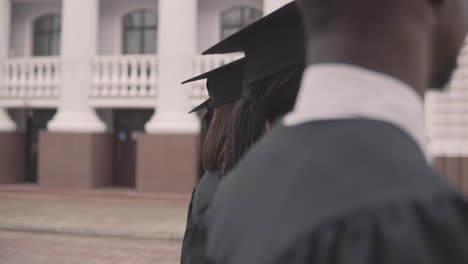 linda estudiante de posgrado en bata y gorra en una fila mirando a la cámara y sonriendo