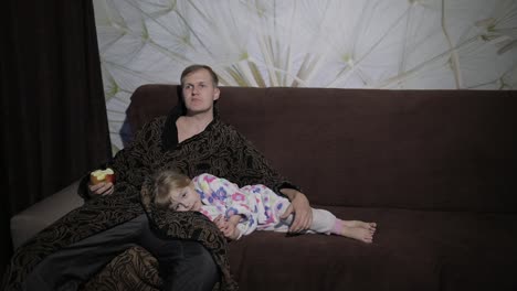 small daughter with her father watching interesting film and eating apple