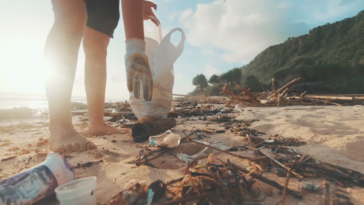 젊은 백인 여성 자원봉사자는 바다의 모래에서 꺼기를 수집하고 가방에 넣습니다.
