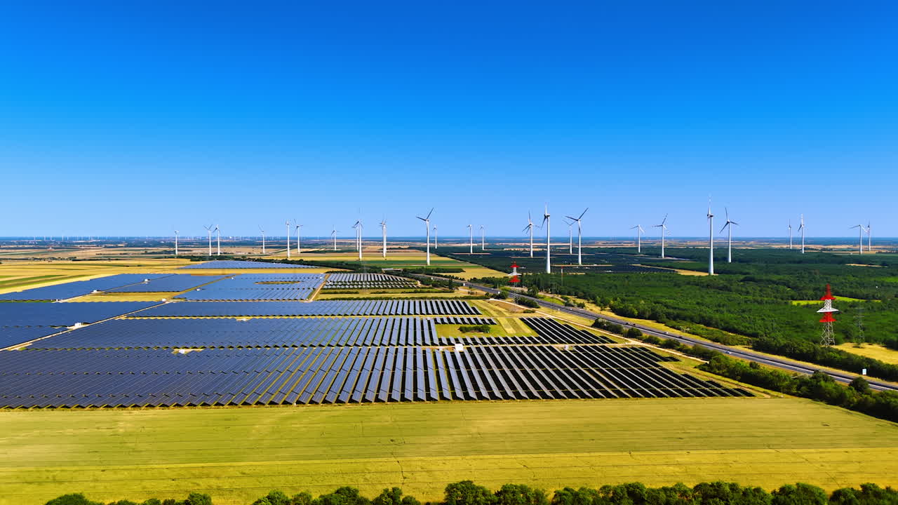 Sites of solar panels installed in the agricultural fields. Wind farms work at backdrop. Aerial view