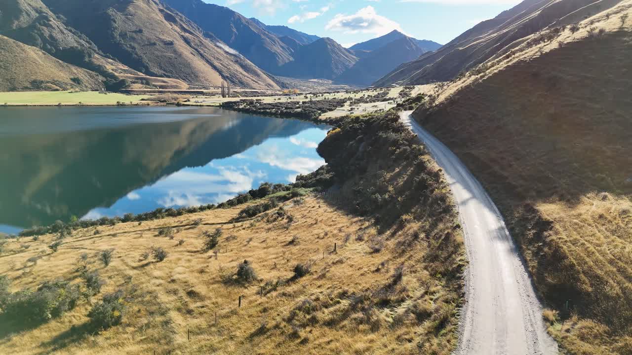 Aerial view of a car driving along a winding road beside Lake Moke, surrounded by mountains under clear skies