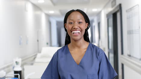 Portrait-of-happy-african-american-female-doctor-wearing-scrubs-in-hospital,-slow-motion