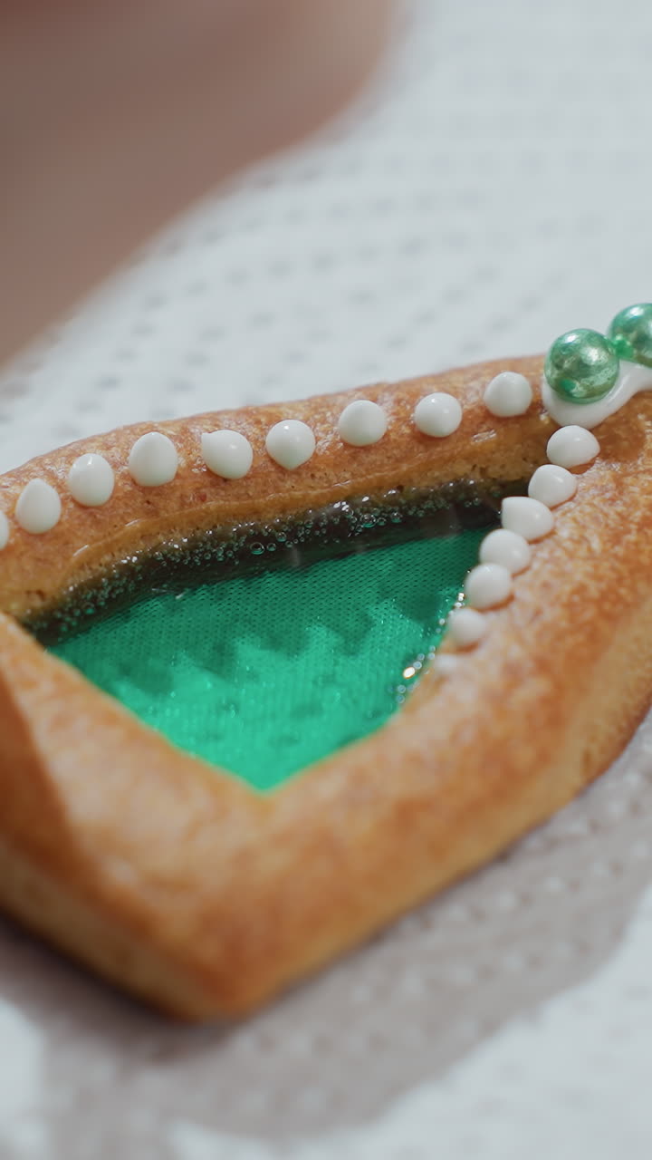 Close-up of cookie decoration in progress with white icing and green beads, cookie with intricate piping details placed on white tissue paper, showcasing meticulous baking