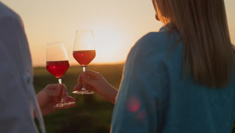 Hände-Mit-Champagnergläsern-Klirren-Vor-Der-Kulisse-Einer-Malerischen-Landschaft,-In-Der-Die-Sonne-Untergeht