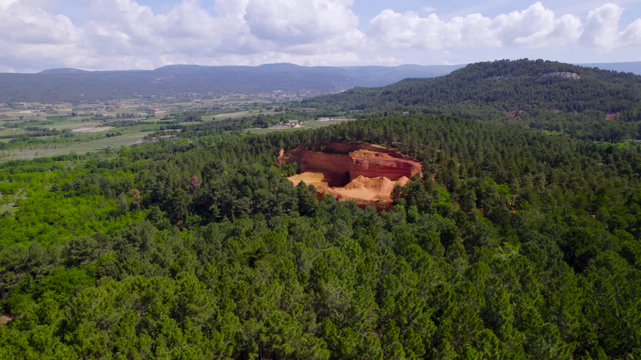 vista aérea con drones de una colina llena de árboles, una cantera rocosa clara y naranja llamada "mine de bruoux", en un gran valle