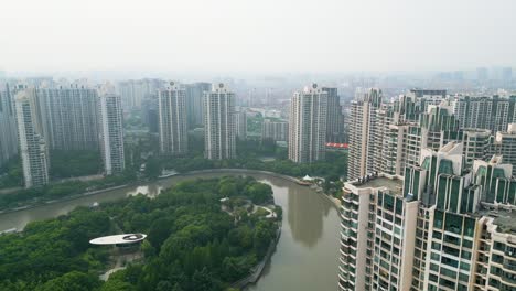 Aeria-tilt-up-reveal-of-green-recreational-park-and-curved-canal-at-the-middle-of-residantial-buildings-at-Pu-Tuo-Qu-district-Shanghai,-China