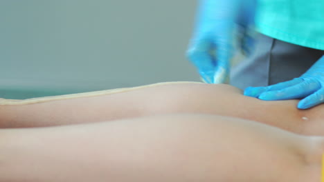 two girls in a beauty salon master in a bathrobe and gloves doing the procedure to remove hair on the legs with a sugar mixture