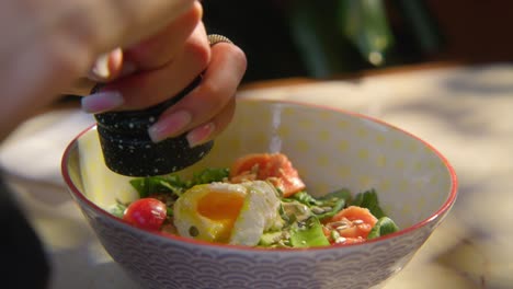 woman seasoning a healthy salad with poached egg and vegetables