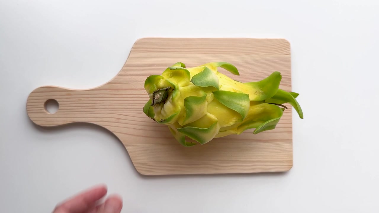 Persona che posiziona un frutto del drago giallo fresco su un tagliere di legno