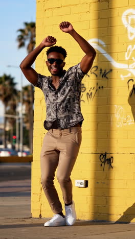 happy man dancing against a yellow graffiti wall