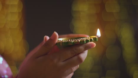 close up of woman holding lit diya oil lamp to celebrate festival of diwali