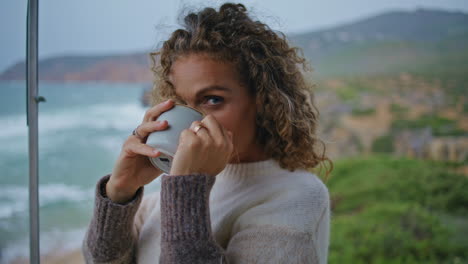 pretty lady enjoy tea at cloudy ocean coast closeup. curly woman drinking coffee