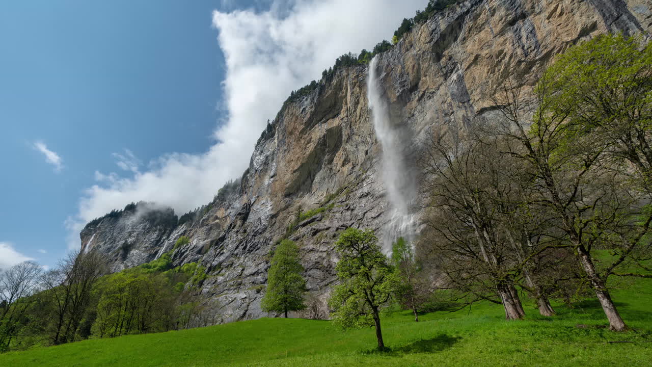 timelapse, cachoeira, penhascos íngremes e nuvens se movendo acima da paisagem verde dos alpes suíços
