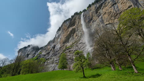 timelapse, waterfall, steep cliffs and clouds moving above green landscape of swiss alps