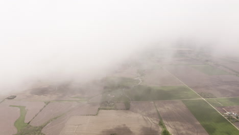 aerial drone moves through clouds above grassland and farmland in midwest of united states