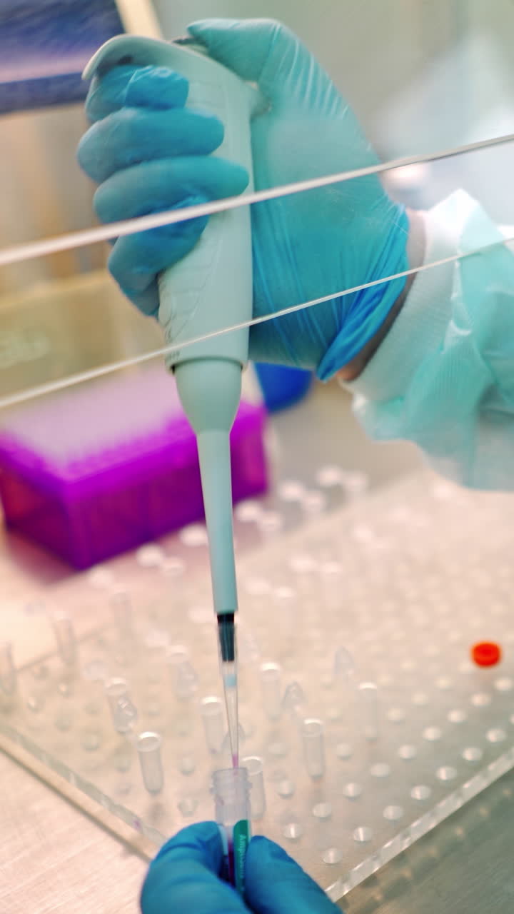 Medical assistant works with test tubes. Researcher in protective uniform dripping liquid into vials with special instrument. Close-up. Vertical video