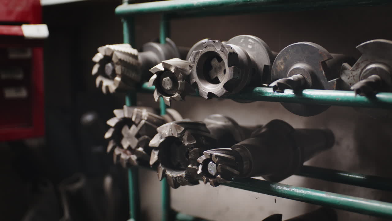 Detailed view of sharp, used steel milling cutters and end mills organized on a metal shelf in a machine shop